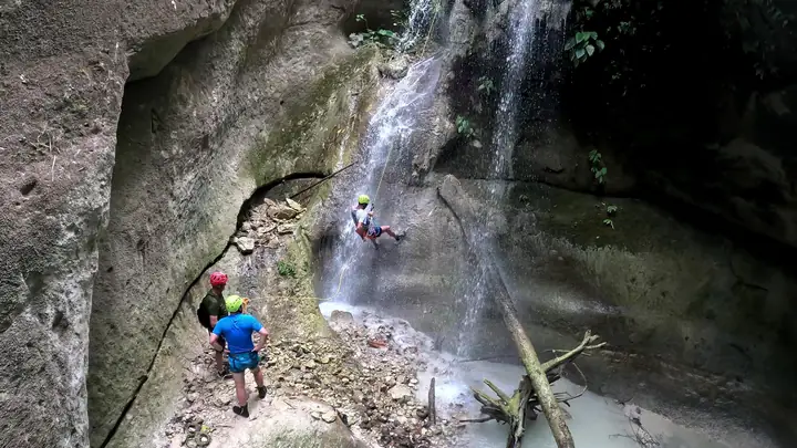 Two guides watching a guest rappel down a waterfall inside the canyon