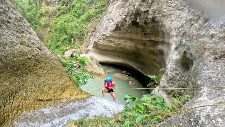Guest in a blue helmet rappelling toward a cave pool