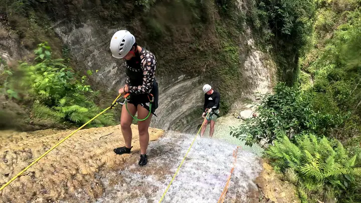 Two guests on rope at the top of the falls above the round pool